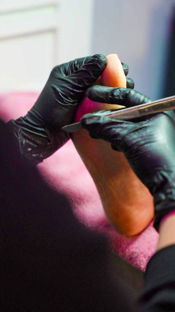 Pedicure met zwarte handschoenen werkt een hiel bij op een roze handdoek
